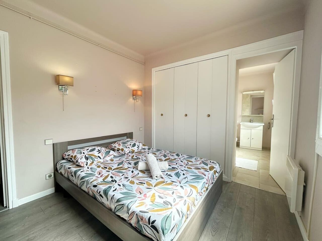 Een slaapkamer met een bed, een nachtkastje, een wandlamp en een deur naar een badkamer.
