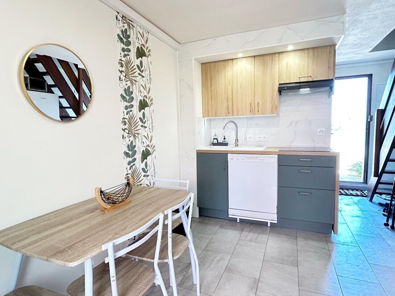 A compact kitchen with a wooden table, white chairs, a white dishwasher, and a small countertop.