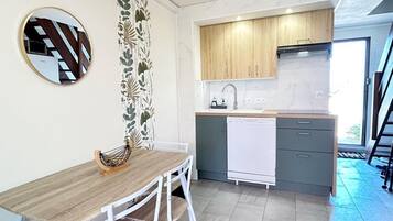 A compact kitchen with a wooden table, white chairs, a white dishwasher, and a small countertop.