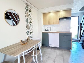 A compact kitchen with a wooden table, white chairs, a white dishwasher, and a small countertop.
