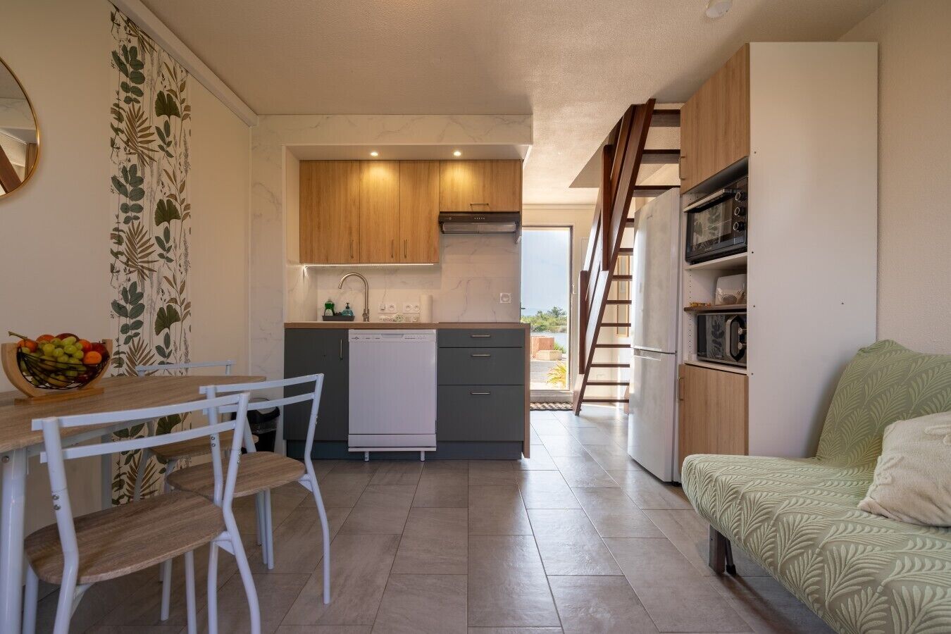 Cocina compacta con lavavajillas, armarios de madera y comedor con mesa y sillas.