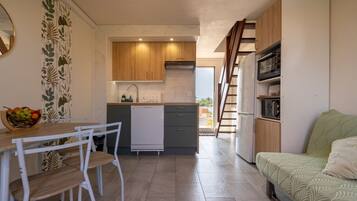 Cocina compacta con lavavajillas, armarios de madera y comedor con mesa y sillas.