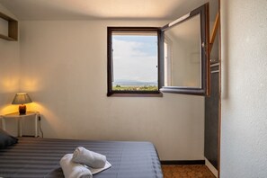 A hotel room with a bed, a nightstand with a lamp, a window with a view of the landscape, and a door.