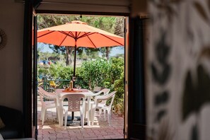 An outdoor patio with a table and chairs, an umbrella, and a view of greenery. - House for 5 people • Swimming Pool • Beach within walking distance • Air Conditioning (Le Barcarès)
