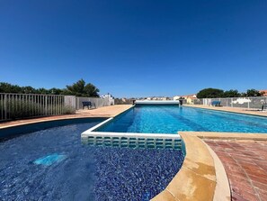 A rectangular swimming pool with a tiled edge, surrounded by a fence and a brick deck.