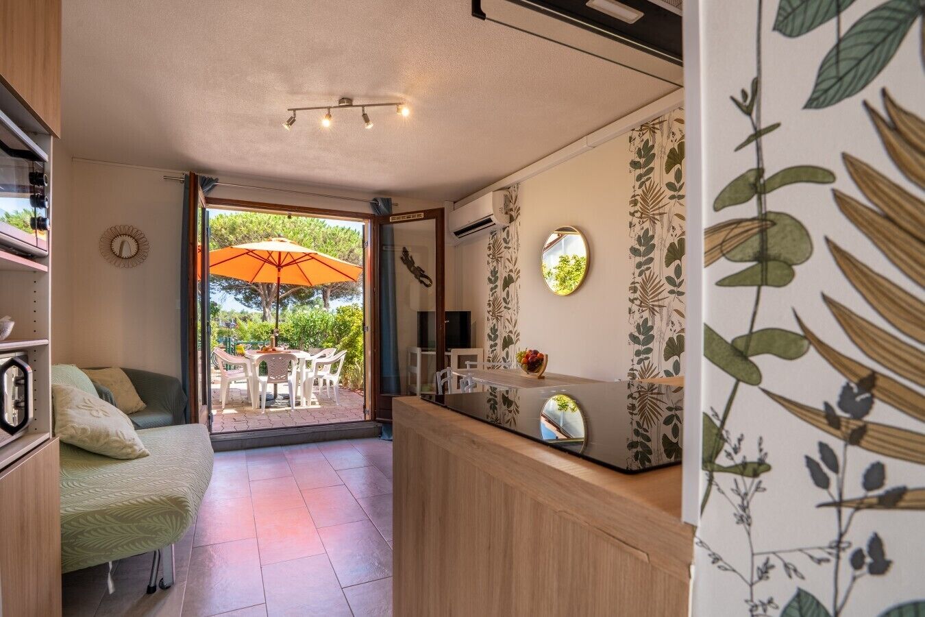 Une pièce compacte comprenant un lit, un coin repas avec un parasol, un comptoir de cuisine et une vue sur l’extérieur.