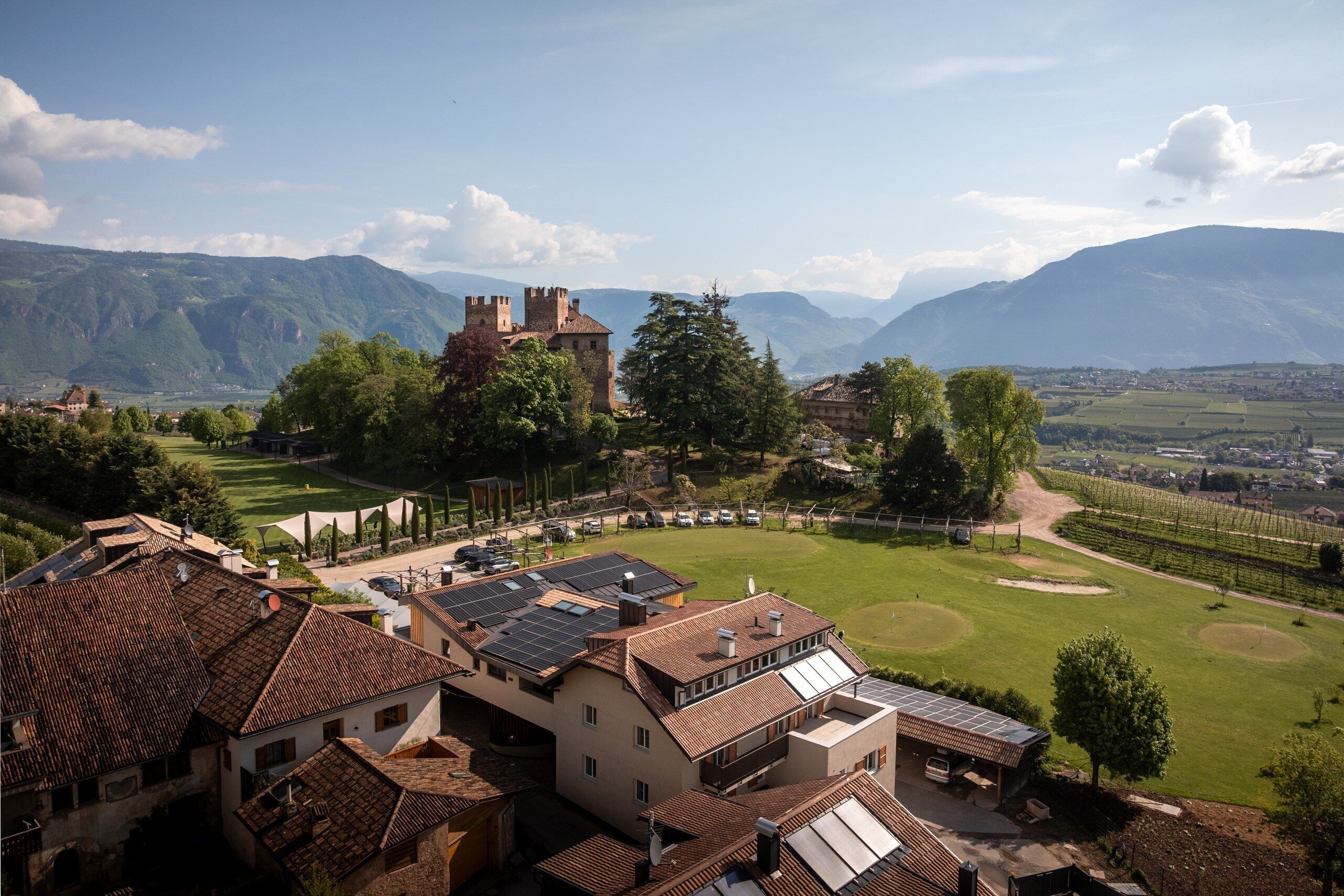 A historic building with a castle-like structure, surrounded by lush greenery and mountains in the background.