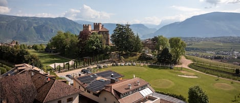 A historic building with a castle-like structure, surrounded by lush greenery and mountains in the background.