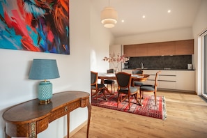 Une cuisine moderne avec des meubles en bois, un coin repas agrémenté d’un tapis rouge et une lampe bleue posée sur une console en bois.