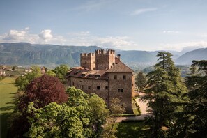 Eine historische Steinburg mit Zinnen, umgeben von üppiger Vegetation und Bergen im Hintergrund.