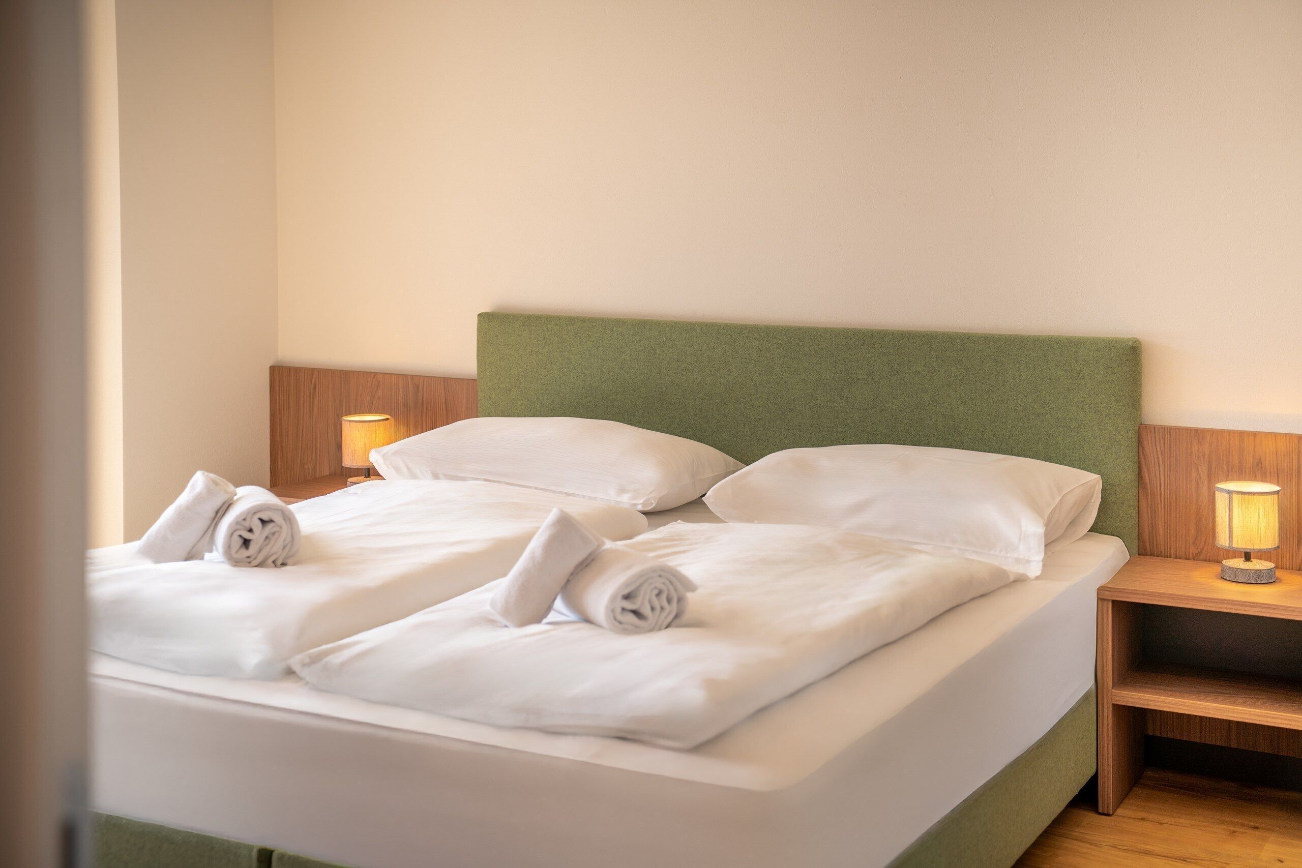 Ein ordentlich bezogenes Bett mit weißen Leinen und Kissen, zwei Nachttischlampen und ein Nachttisch aus Holz.