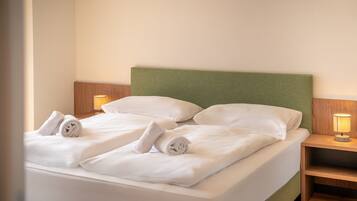 A neatly made bed with white linens and pillows, two bedside lamps, and a wooden nightstand.