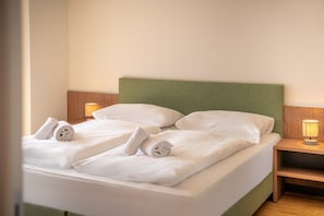 Un lit bien fait, avec du linge de lit blanc et des oreillers, deux lampes de chevet et une table de nuit en bois.