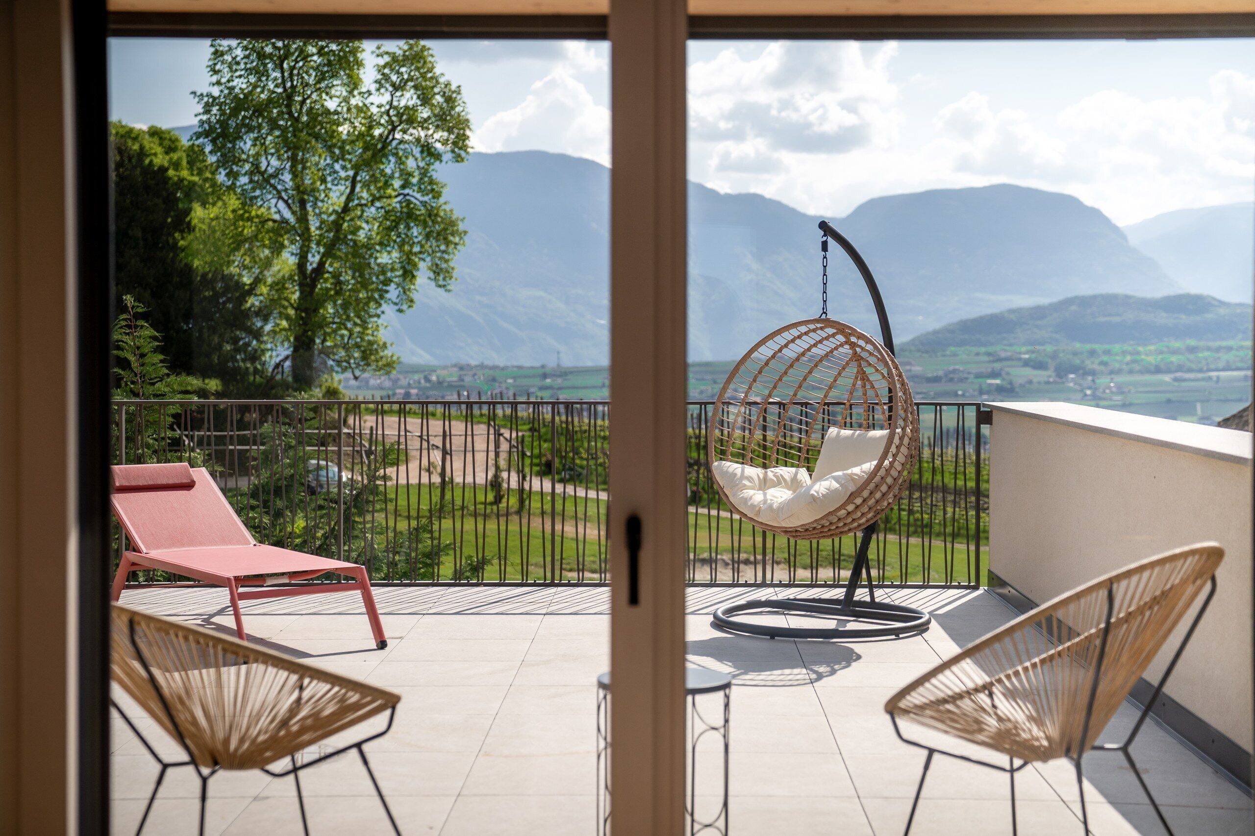 Ein Balkon mit Hängesessel, einem roten Liegestuhl und Blick auf Berge.