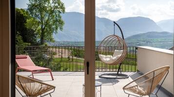 A balcony with a hanging chair, a red lounge chair, and a view of mountains.