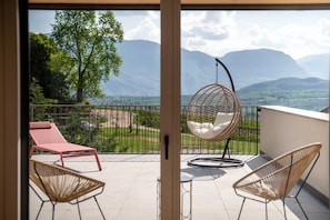 Un balcon avec un fauteuil suspendu, un fauteuil de relaxation rouge et une vue sur les montagnes.