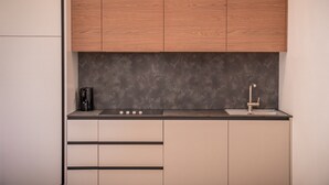 Uma cozinha compacta com armários de madeira, uma bancada escura, cafeteira e uma torneira moderna.