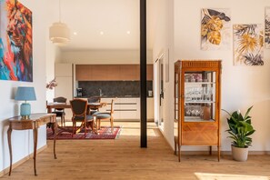Une cuisine moderne avec des meubles en bois, un coin repas avec des chaises, un meuble vitré contenant de la vaisselle et un grand tableau accroché au mur.