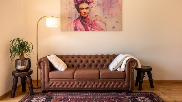 A room with a brown leather sofa, a potted plant, a floor lamp, and a painting on the wall. - Vintonia Panorama Apartments I 740A Gleif (Appiano sulla strada del vino)
