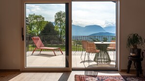 A room with a sliding glass door leading to an outdoor deck with a table and chairs, a red lounge chair, and a potted plant. - Vintonia Panorama Apartments I 740A Gleif (Appiano sulla strada del vino)