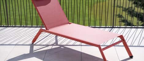 Un fauteuil rouge est placé sur un balcon doté d’une rambarde en métal, d’où l’on peut admirer une pelouse verdoyante.