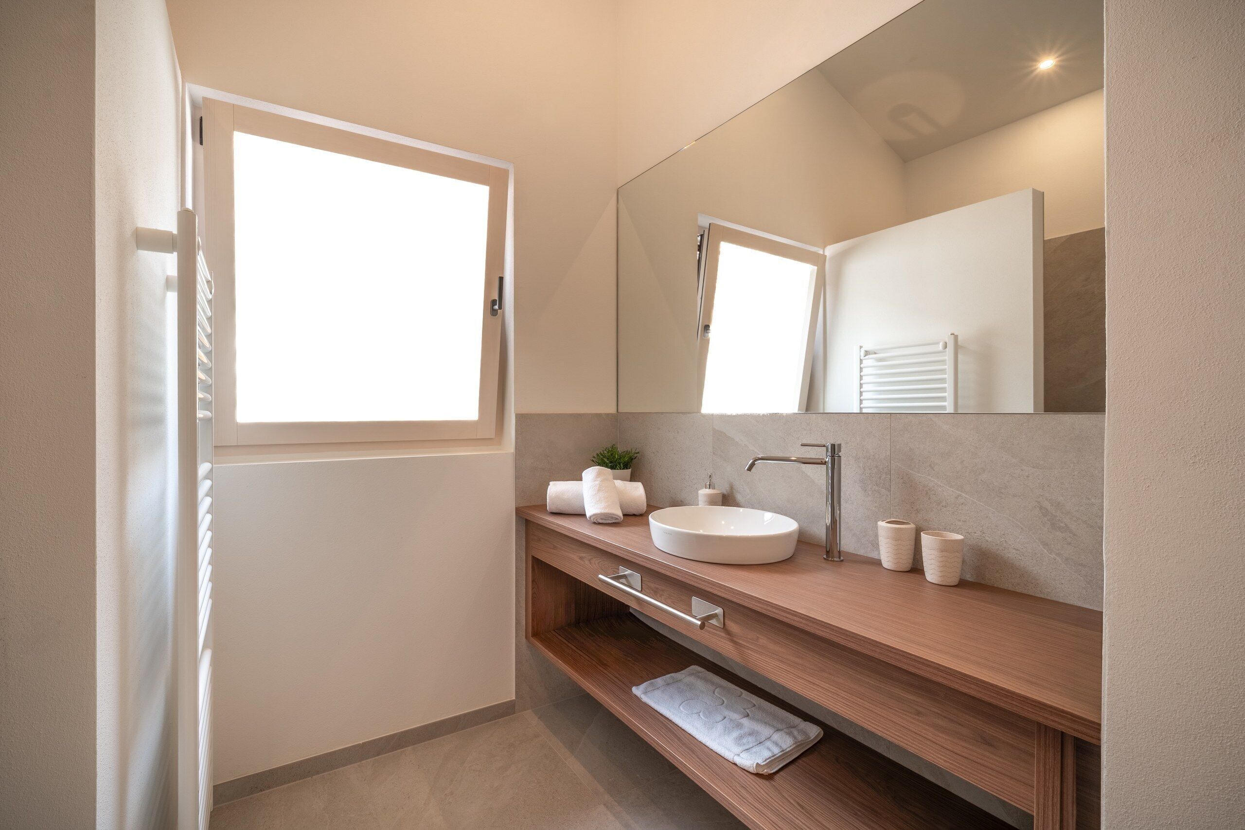 Un baño moderno con un ventanal grande, un lavamanos, un espejo y un perchero para toallas.