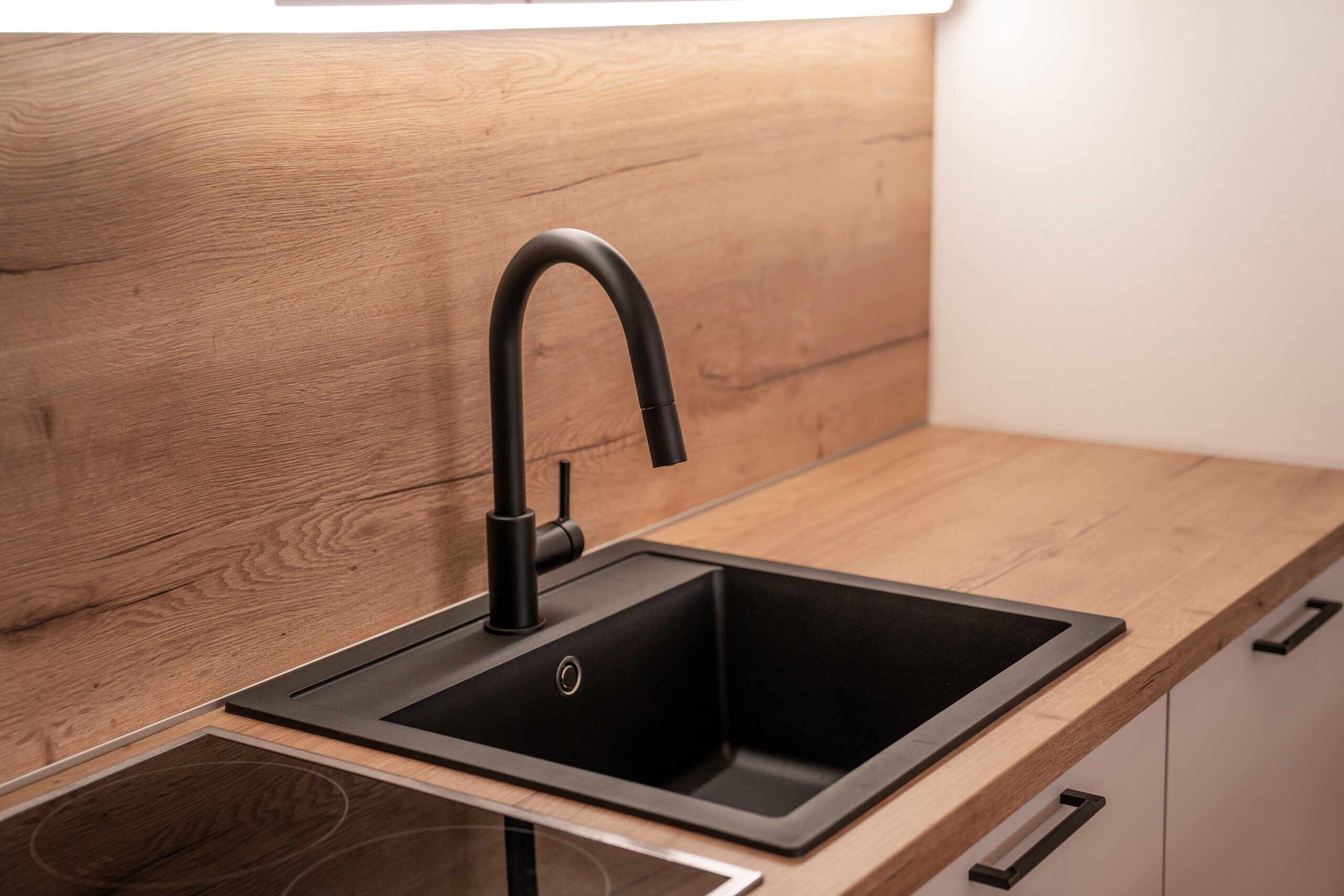 Eine moderne Küche mit einem schwarzen Wasserhahn, einer Holz Arbeitsplatte und einem Edelstahl-Spülbecken.