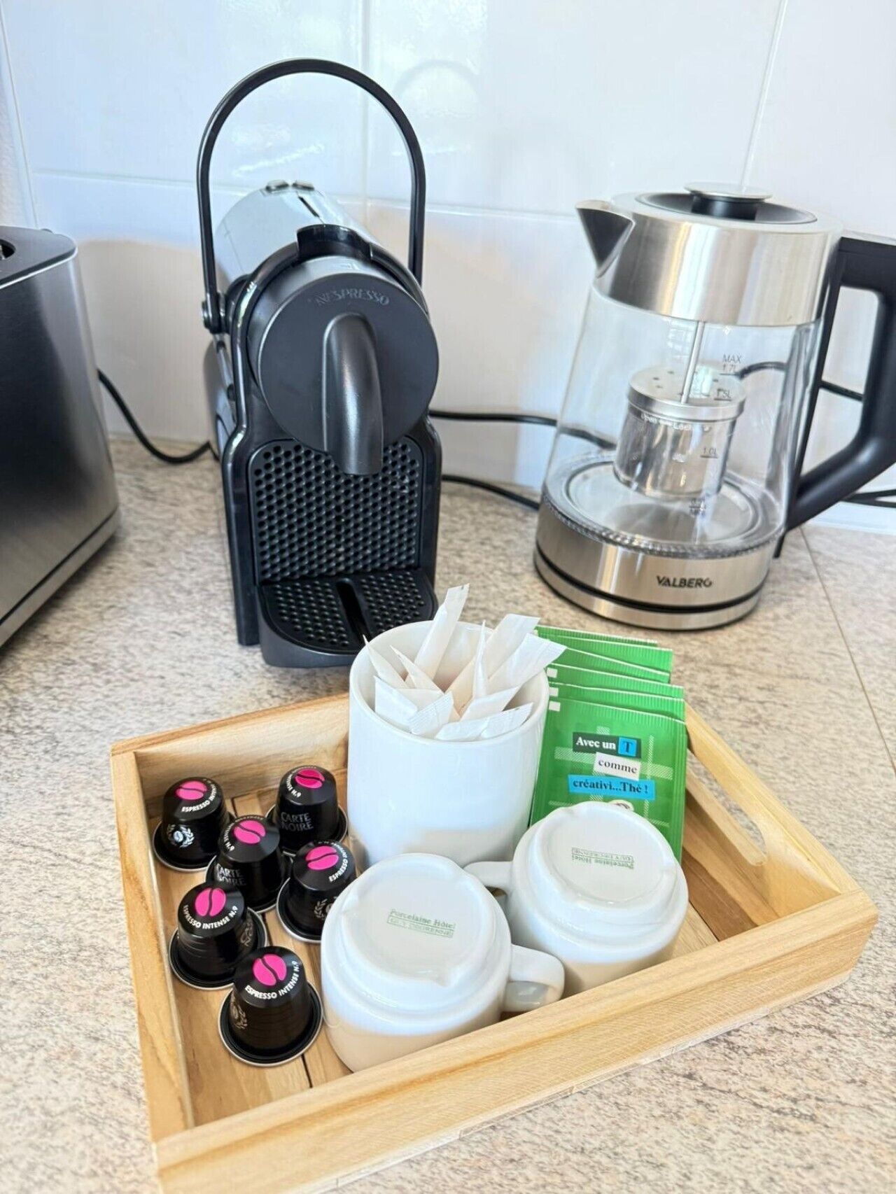 Una encimera de cocina con una cafetera, una jarra de café y una bandeja con cápsulas de café y una taza.