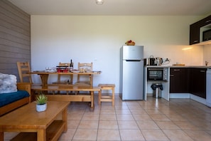 A compact kitchen with a refrigerator, microwave, oven, and a dining area with wooden furniture.