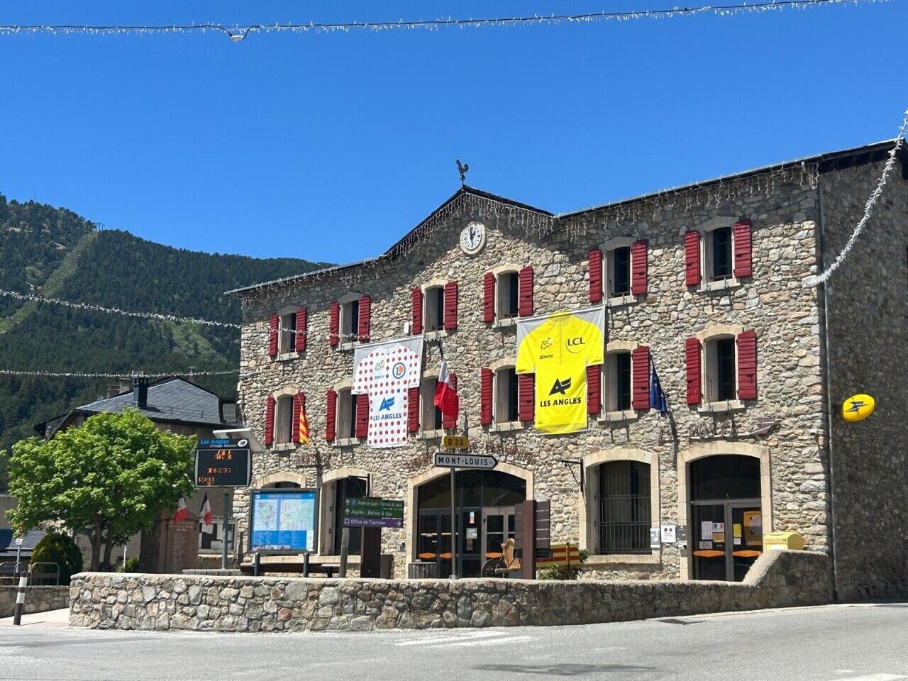 Un bâtiment en pierre avec des volets rouges, une horloge et plusieurs drapeaux.