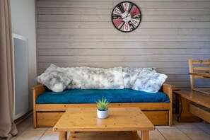 En soffa i trä med en blå kudde, en mjuk grå filt och en liten krukväxt på ett träbord.