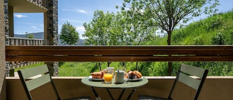 A balcony with two chairs, a table, and breakfast items including croissants, juice, and coffee.