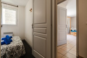 A bedroom with a bed, a window, and a door leading to another room.