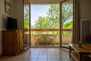A balcony with a table and chairs, a television on a cabinet, and a poster on the wall.