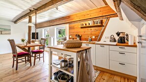 Una cocina rústica con vigas de madera, un comedor con mesa y sillas de madera, y vistas al verdor exterior.