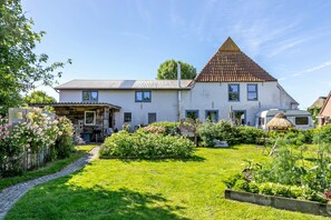 A white house with a brown roof, a garden with various plants, and a thatched-roof structure. - Apartment Klein Bullerbü in Schülp an der Nord Sea with Shared Terrace, Garden and Wi-Fi (Schülp)