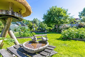 A garden with a wooden bench, a bird bath, and a thatched structure. - Apartment Klein Bullerbü in Schülp an der Nord Sea with Shared Terrace, Garden and Wi-Fi (Schülp)