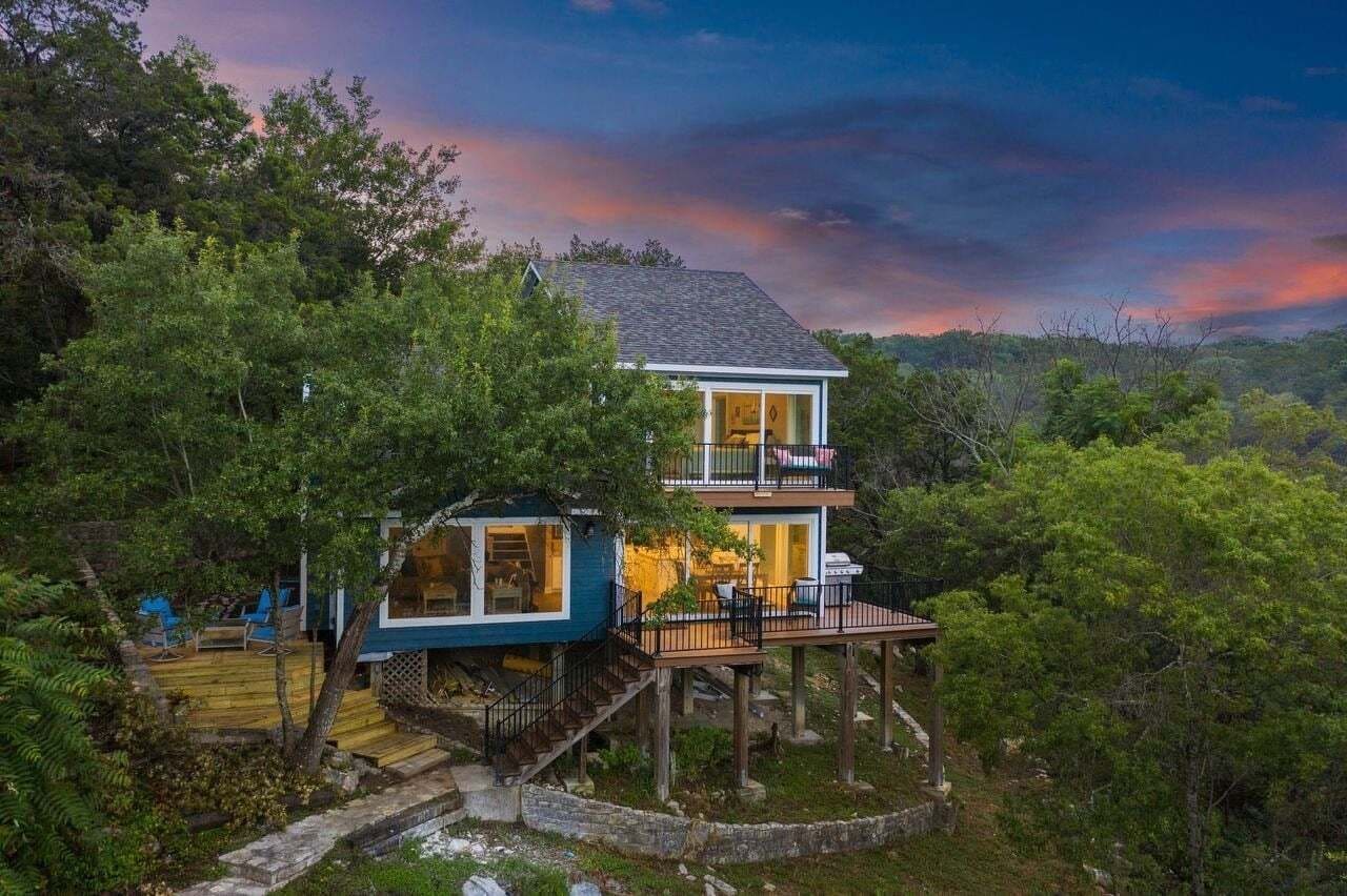 Una casa de dos pisos con un balcón, rodeada de árboles.