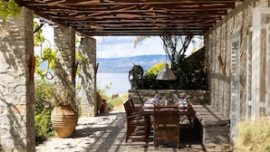 Ein Essbereich im Freien mit Steinmauern, einer Pergola und Blick aufs Meer.