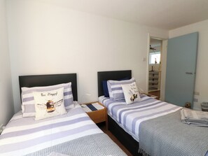 Ein Schlafzimmer mit zwei Betten, jeweils mit gestreifter Bettdecke und Kissen, einem Nachttisch und einer Tür zu einem Badezimmer.