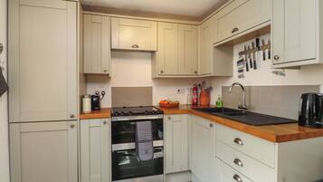 A compact kitchen with a stove, oven, sink, and wooden countertop.