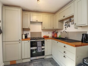 A compact kitchen with a stove, oven, sink, and wooden countertop. - Scoops Nook (Caernarfon)