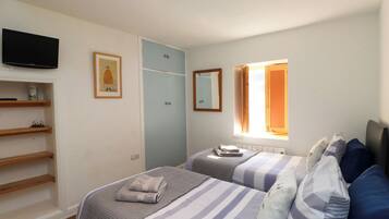 A bedroom with two beds, a TV, a wardrobe, a window with curtains, and a shelf with items.