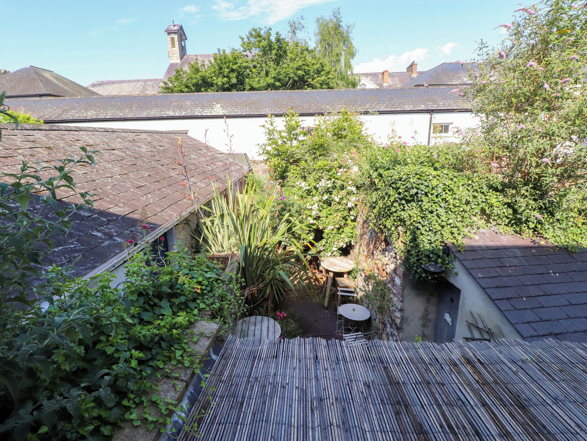 A courtyard with a small table and chairs, surrounded by dense foliage and a wooden fence.