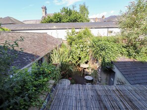 A courtyard with a small table and chairs, surrounded by dense foliage and a wooden fence. - Scoops Nook (Caernarfon)