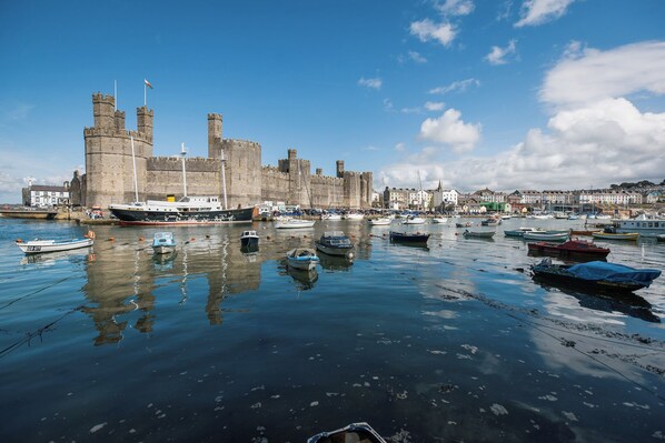 A historic castle with a moat, surrounded by a harbor with various boats. - Scoops Nook (Caernarfon)
