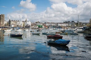 A harbor with numerous boats docked, a historic building on the left, and a row of colorful houses in the background. - Scoops Nook (Caernarfon)