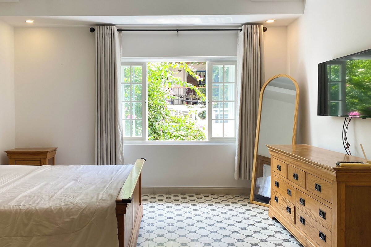A bedroom with a bed, a dresser, a mirror, and a window with curtains.