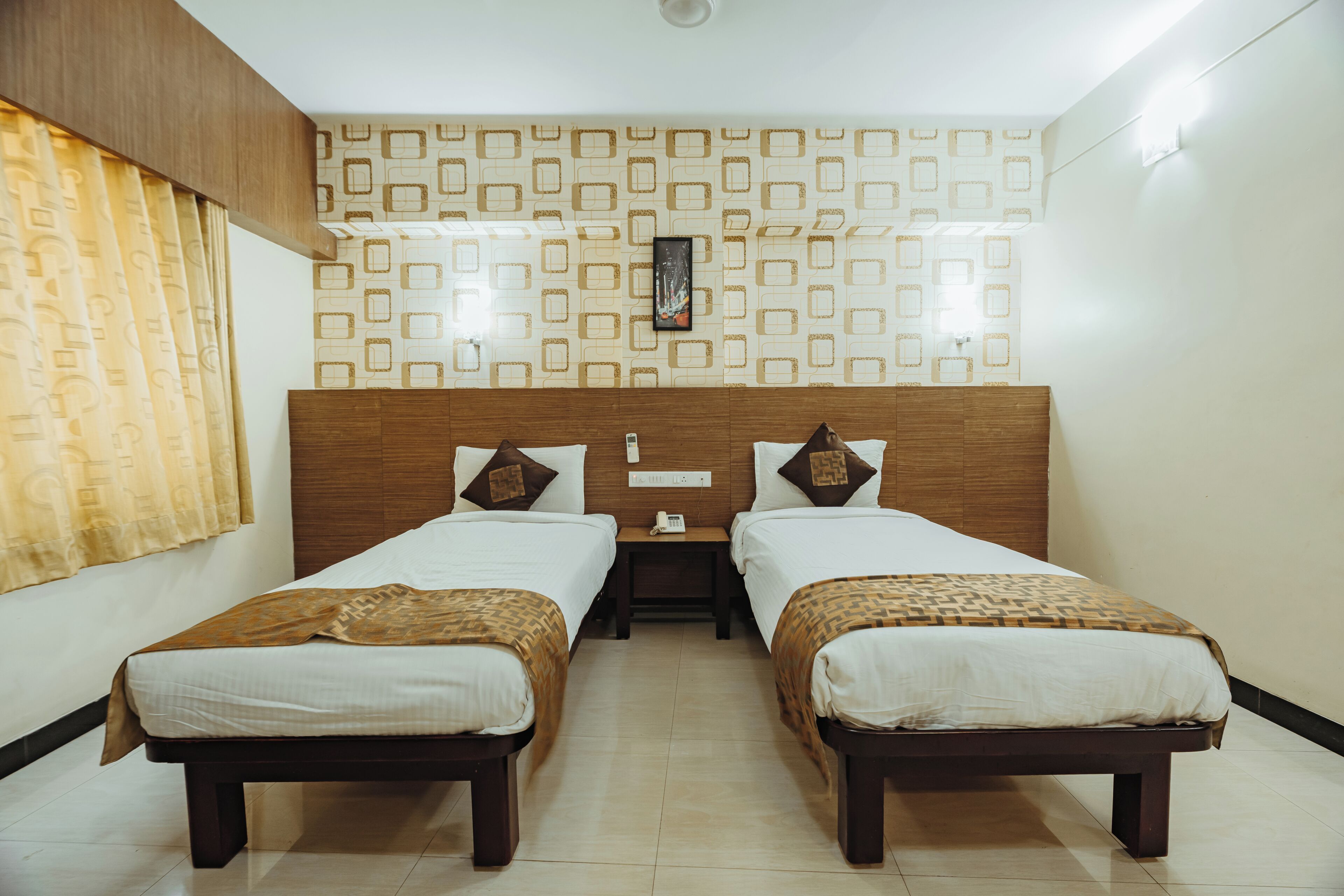 Een hotelkamer met twee eenpersoonsbedden, een houten hoofdbord, een behang met patroon en een nachtkastje met een telefoon.