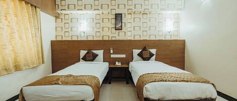A hotel room with two single beds, a wooden headboard, a patterned wall, and a nightstand with a phone.